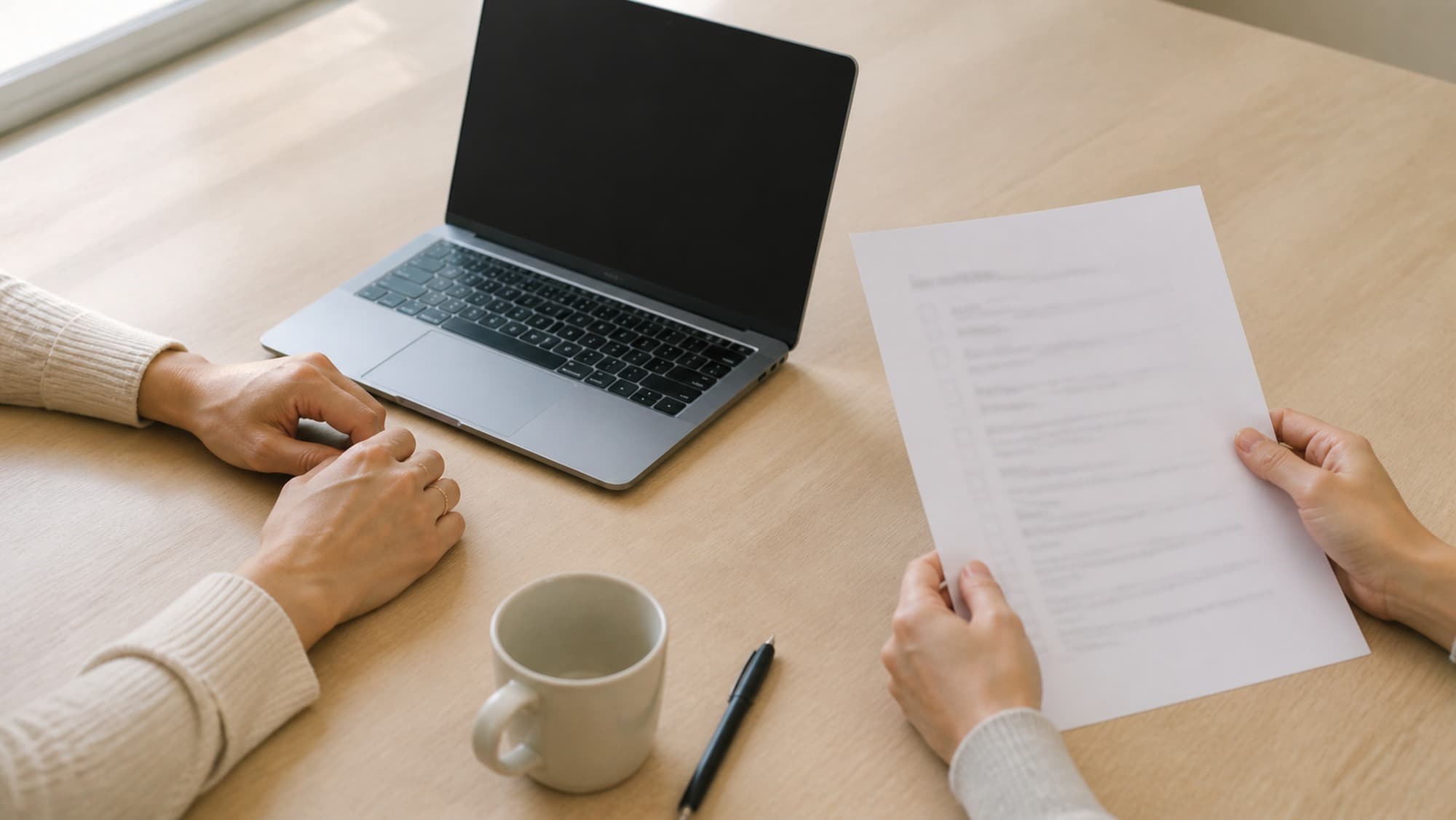 Two people at a table, one beside a laptop and one holding a printed checklist.